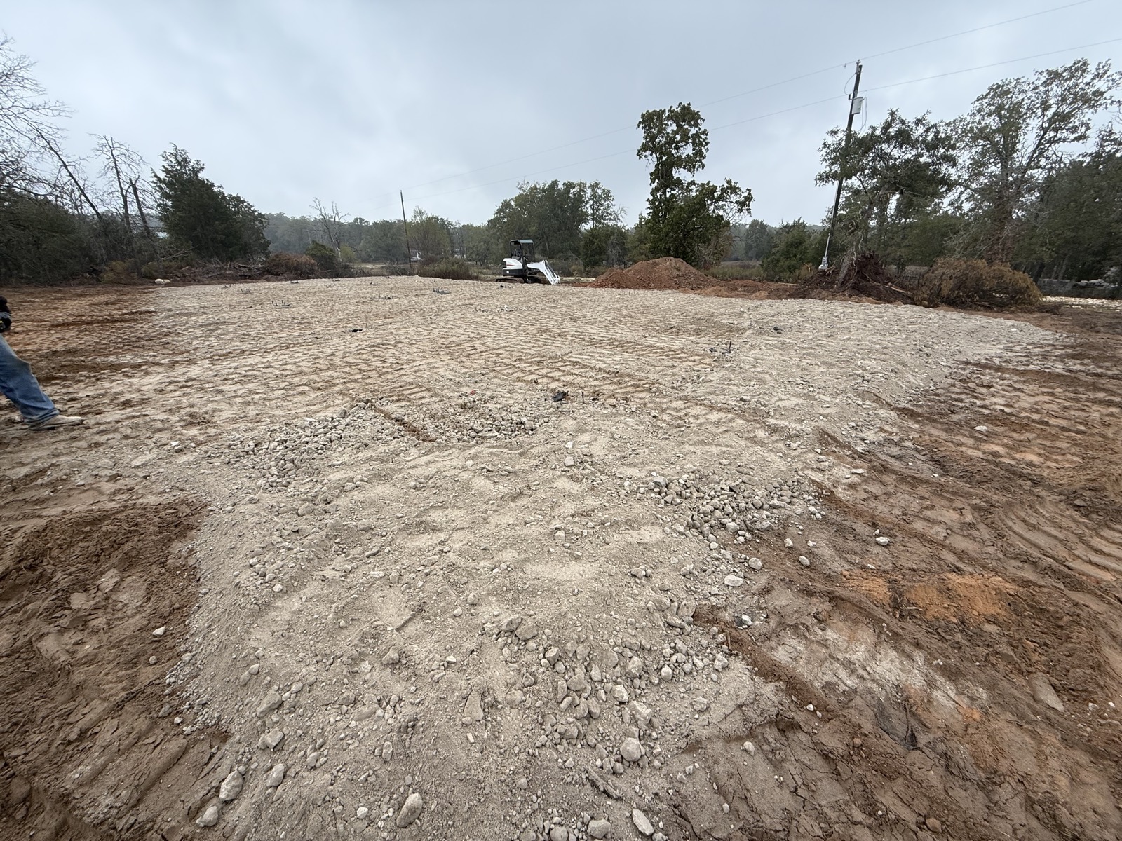 Finished pad graded and compacted, mini excavator at the tree line